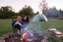 Mutter und Tochter sitzen am Lagerfeuer und kochen Wurst über dem Feuer — Stockfoto