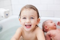 Toddler girl in bath with infant sister — Stock Photo