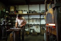 Metalúrgico macho martillando metal en yunque de taller - foto de stock