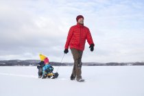 Father pulling sons along on sledge in snow covered landscape — Stock Photo