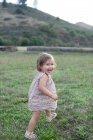 Linda niña corriendo en el campo mirando por encima de su hombro - foto de stock