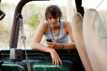 Adolescente apoyado contra jeep chequeo de teléfono - foto de stock