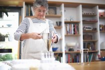 Femme âgée utilisant entonnoir à crêpes pour verser le mélange dans des pots en plastique — Photo de stock
