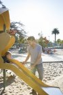 Pai assistindo jovem filho no playground slide — Fotografia de Stock