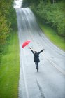 Visão traseira da mulher na estrada vazia com guarda-chuva vermelho — Fotografia de Stock
