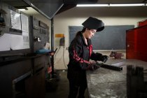Metalsmith femminile esaminando asta metallica al banco di officina — Foto stock