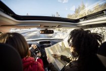 Mujer conduciendo coche, amigo en el asiento del pasajero mirando el mapa - foto de stock