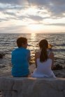 Adolescente casal assistindo por do sol sobre o mar — Fotografia de Stock