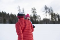 Pai carregando jovem filho na neve paisagem coberta — Fotografia de Stock