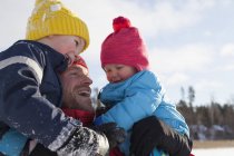 Padre che tiene giovani figli, sorridente, in ambiente invernale — Foto stock