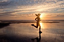 Woman running on beach at sunrise — Stock Photo