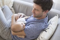 Padre che si rilassa sul divano, tenendo in braccio il bambino — Foto stock