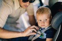 Отец обеспечивал безопасность маленького сына на автокресле — стоковое фото