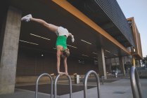 Young woman doing handstand on metal bar in urban environment — Stock Photo