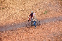 Couple vélo sur le chemin à travers les feuilles — Photo de stock