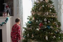 Мальчик за рождественской ёлкой смотрит в окно — стоковое фото
