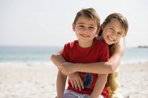 Hermano y hermana abrazándose en una playa - foto de stock