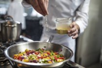 Шеф-кухар приправляє сковороду овочів на плиті, крупним планом — стокове фото