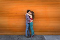 Romantic couple kissing in front of orange shutter — Stock Photo