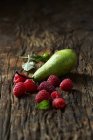 Pear and raspberries on old wooden surface — Stock Photo