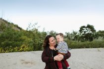 Mother on beach holding smiling baby boy — Stock Photo