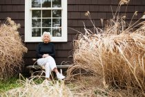 Portrait of senior woman sitting on bench outside house — Stock Photo