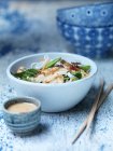 Bowl of spicy peanut chicken, satay sauce, fresh vegetables and noodles with chopsticks on blue surface — Stock Photo