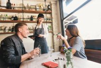 Female bartender serving young couple in cocktail bar — Stock Photo