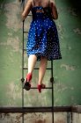 Вид сзади на женщину в платье и на высоких каблуках, лестницу для скалолазания — стоковое фото