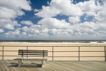 Panchina sul lungomare con spiaggia sabbiosa e cielo nuvoloso — Foto stock