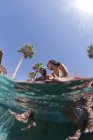 Jovem casal sentado na borda da piscina, vista de nível de superfície — Fotografia de Stock