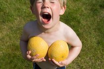 Niño sosteniendo mitades de melón - foto de stock