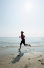 Mujer corriendo en la playa en un día soleado - foto de stock