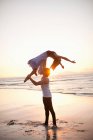 Jovem homem levantando parceiro de dança na praia iluminada pelo sol — Fotografia de Stock