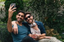 Junges männliches Paar sitzt im Garten und macht Smartphone-Selfie — Stockfoto