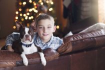 Portrait of young boy sitting on sofa with dog — Stock Photo