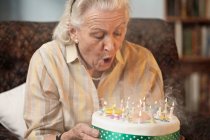 Seniorin pustet Geburtstagskerzen aus — Stockfoto