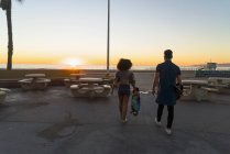 Paar geht in Strandnähe, hält Skateboards in der Hand, Rückansicht — Stockfoto