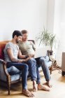 Male couple sitting on sofa, looking at laptop — Stock Photo