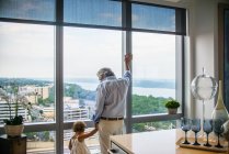 Grandfather holding granddaughter's hand looking out of window at home — Stock Photo