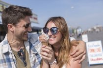Zeitgenössisches Paar amüsiert sich auf der Uferpromenade des Vergnügungsparks und isst Softeis — Stockfoto