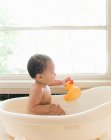 Baby girl sitting in bath holding rubber duck — Stock Photo