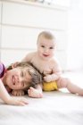 Portrait de bébé fille heureuse tirant les cheveux grand frère sur le lit — Photo de stock