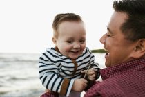 Father on beach holding smiling baby boy — Stock Photo