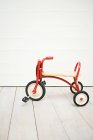 Red small tricycle with wheels on wooden floor at home — Stock Photo