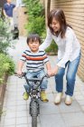 Madre ayudando a su hijo a montar en bicicleta - foto de stock