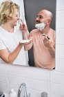 Зеркало в ванной изображает мужскую пару, дурачащуюся во время бритья — стоковое фото