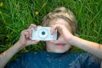 Хлопчик лежить на траві фотографується за допомогою смартфона — стокове фото