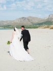 Bride and groom walking on beach — Stock Photo