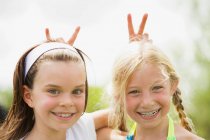 2 молодые девушки улыбаются давая кролика уши — стоковое фото